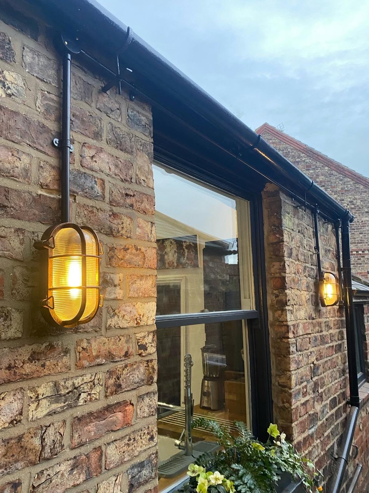 Brass bulkhead wall lights glowing on a brick extension