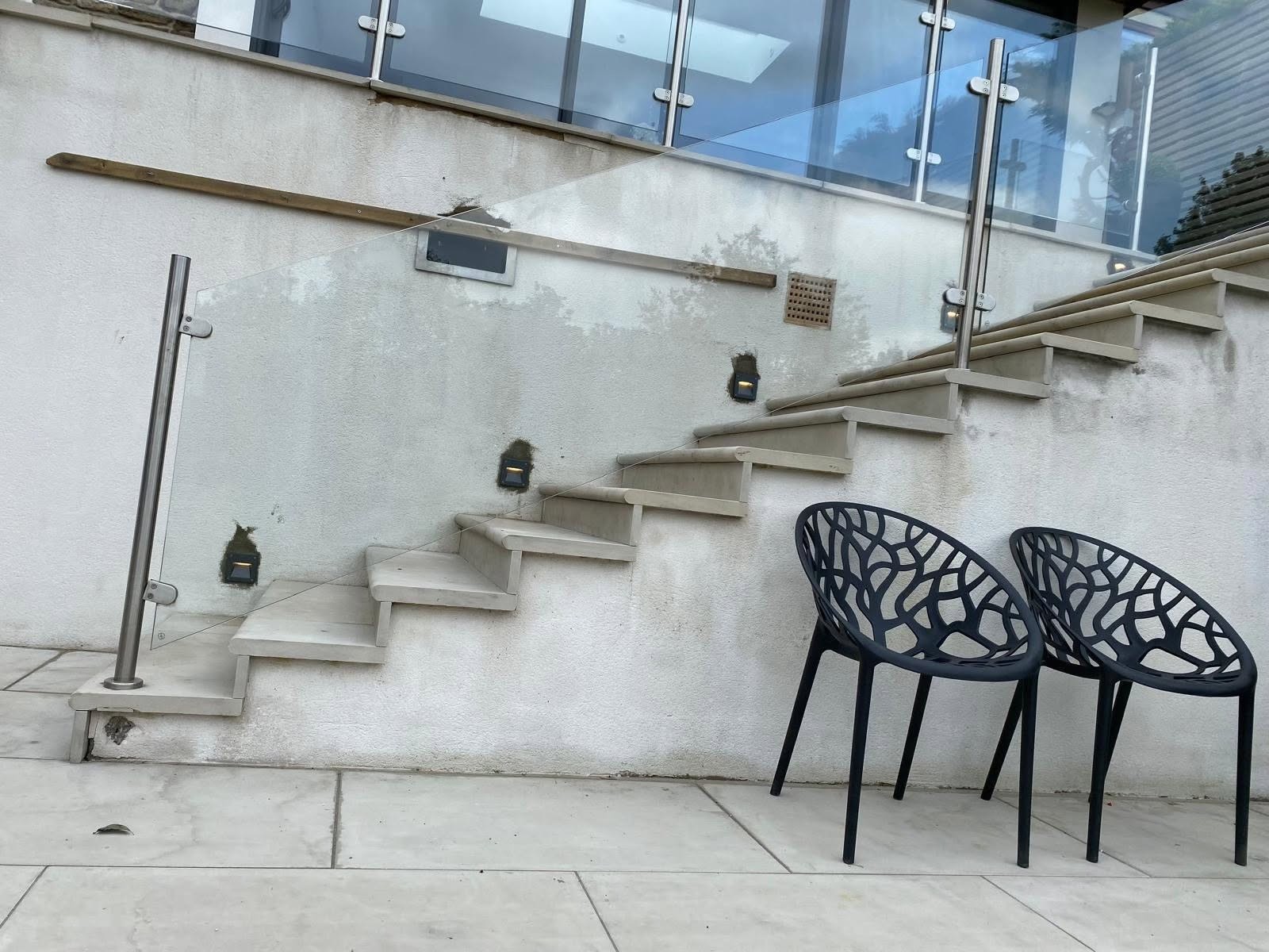 Garden steps with small lights set into the riser wall, beside a glass balustrade
