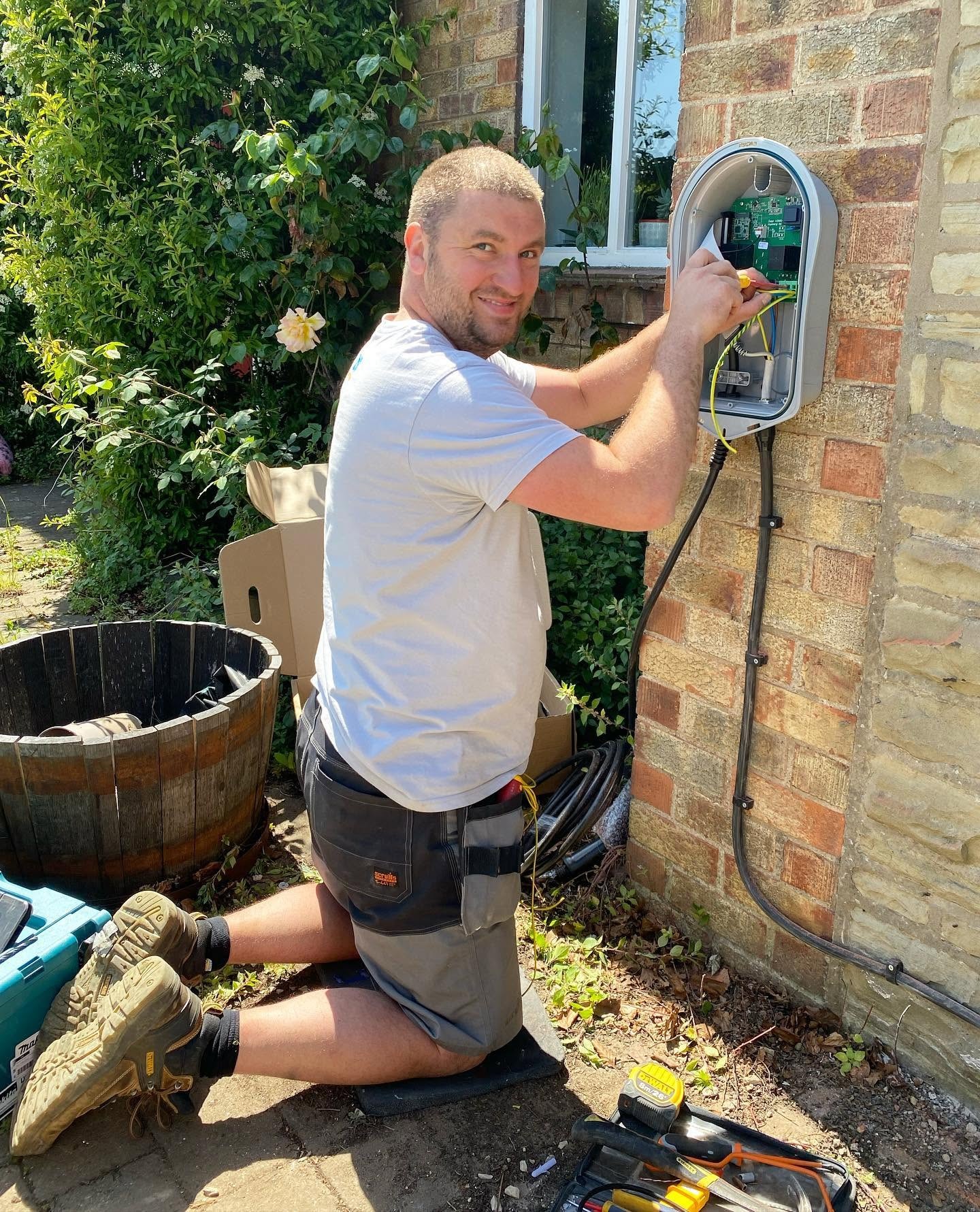 Tom kneeling to wire an outdoor wall-mounted unit on a stone house