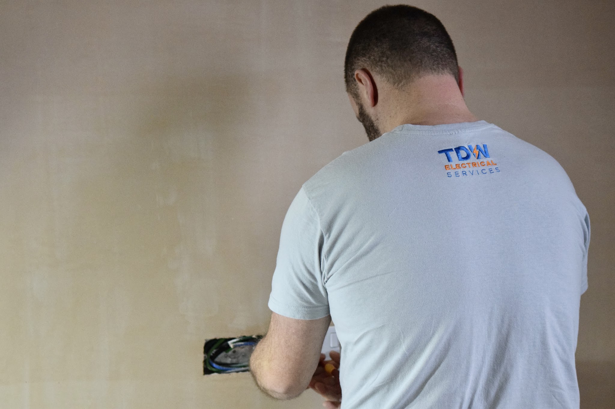 Tom, with the TDW logo on his T-shirt, working at a socket box in a wall